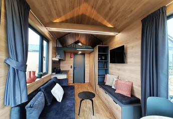 Modernes, helles Wohnzimmer in einem Tiny House am Gulperberg, Niederlande, mit Holzdekor und Sofa.