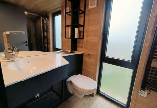 Modernes Bad im Tiny House am Gulperberg, Niederlande, mit Waschbecken, Spiegel, WC und großen Fenstern.