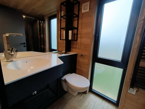 Salle de bain moderne dans Tiny House à Gulperberg, Pays-Bas, avec lavabo, miroir, toilettes et grandes fenêtres.