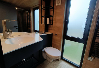 Salle de bain moderne dans Tiny House à Gulperberg, Pays-Bas, avec lavabo, miroir, toilettes et grandes fenêtres.