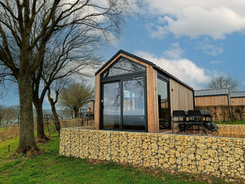 Moderne Tiny House Lodge am Gulperberg in den Niederlanden, umgeben von Bäumen und Steinmauern.