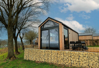 Moderne Tiny House Lodge am Gulperberg in den Niederlanden, umgeben von Bäumen und Steinmauern.