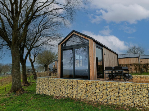 Moderna tiny house lodge a Gulperberg, Paesi Bassi, circondata da alberi, natura e muri di pietra.