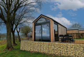 Moderna tiny house lodge a Gulperberg, Paesi Bassi, circondata da alberi, natura e muri di pietra.