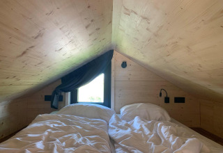 Zolder slaapkamer met tweepersoonsbed en schuin plafond in Tiny House op Gulperberg, Nederland.