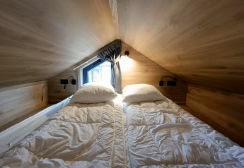 Slaapruimte met twee eenpersoonsbedden in Tiny House op Gulperberg, Nederland, houten muren en dakraam.