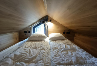 Slaapruimte met twee eenpersoonsbedden in Tiny House op Gulperberg, Nederland, houten muren en dakraam.