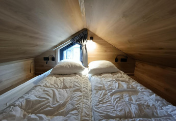 Espace nuit avec deux lits simples dans Tiny House à Gulperberg, Pays-Bas, murs en bois et lucarne.