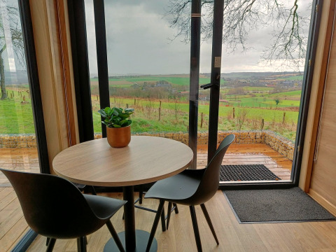 Runder Tisch mit zwei Stühlen und Topfpflanze, Blick auf die grünen Hügel vom Tiny House Gulperberg, Niederlande.