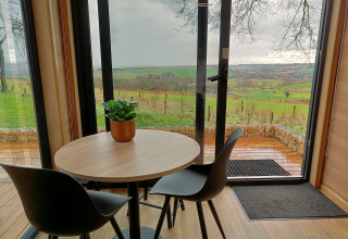 Runder Tisch mit zwei Stühlen und Topfpflanze, Blick auf die grünen Hügel vom Tiny House Gulperberg, Niederlande.