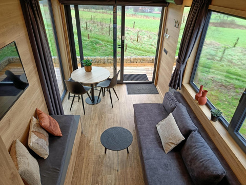 Interior del Tiny House en Gulperberg, Países Bajos, con sofás acogedores, mesa de comedor y grandes ventanales.