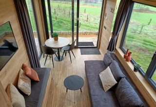 Interni della Tiny House a Gulperberg, Paesi Bassi, con divano, tavolo da pranzo e grandi finestre panoramiche.
