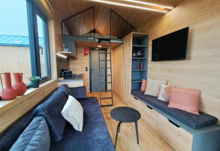 Interno moderno di tiny house al Gulperberg, Paesi Bassi, con soppalco, cucina, divani e TV a muro.