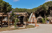 Ferienpark in Andalusien, Spanien, mit Holzhütten, Picknicktischen und Pinienbäumen bei Sonnenschein.