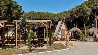 Vakantiepark in Andalusië, Spanje, met houten huisjes, picknicktafels en pijnbomen onder een blauwe lucht.