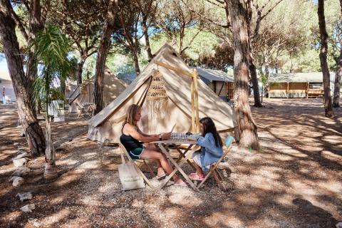 Twee personen spelen een gezelschapsspel aan een tipi-tent bij Glamping Bell Marisma in het bos.