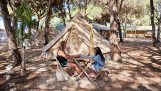 Twee personen spelen een gezelschapsspel aan een tipi-tent bij Glamping Bell Marisma in het bos.