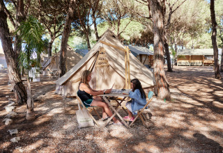 Twee personen spelen een gezelschapsspel aan een tipi-tent bij Glamping Bell Marisma in het bos.