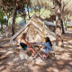 To personer spiller brætspil foran et tipi-telt ved Glamping Bell Marisma i et skovområde med andre telte.