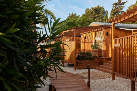 Houten cottages bij TAIGA Conil vakantiepark in Andalusië, Spanje, omringd door planten en zonlicht.
