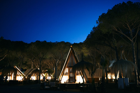 Nächtliche Aufnahme beleuchteter Glamping-Zelte und Holzhäuser im TAIGA Conil Ferienpark, Andalusien.