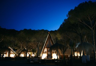 Nachtbeeld van verlichte glamping tenten en houten huisjes in TAIGA Conil vakantiepark in Andalusië, Spanje.