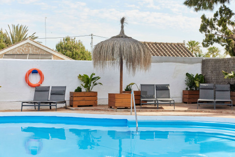 Zwembad met ligstoelen, planten en een rieten parasol bij TAIGA Conil vakantiepark, Andalusië, Spanje.