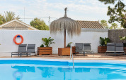 Zwembad met ligstoelen, planten en een rieten parasol bij TAIGA Conil vakantiepark, Andalusië, Spanje.