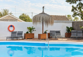 Zwembad met ligstoelen, planten en een rieten parasol bij TAIGA Conil vakantiepark, Andalusië, Spanje.