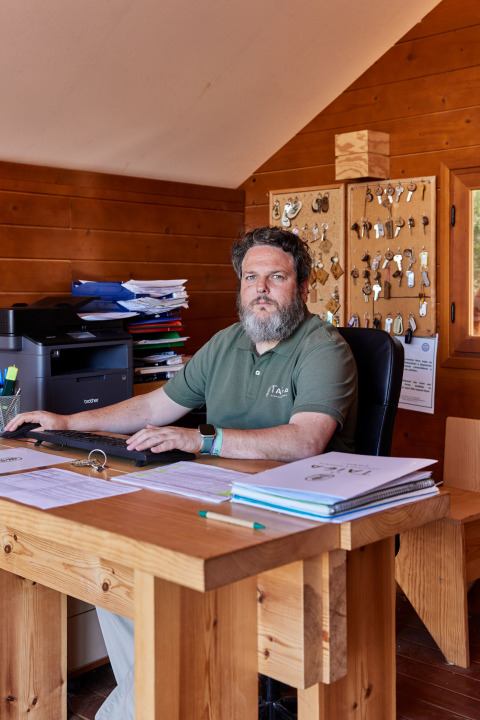 En mand sidder ved et træskrivebord på et kontor med nøgler på væggen i TAIGA Conil, Andalusien.