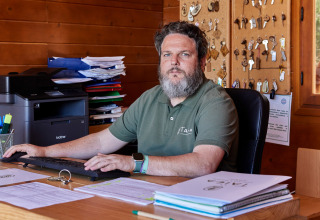 En mand sidder ved et træskrivebord på et kontor med nøgler på væggen i TAIGA Conil, Andalusien.