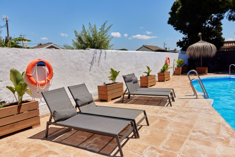 Sonnenliegen am Pool im Ferienpark TAIGA Conil, Andalusien, mit Pflanzen und Rettungsringen dekoriert.