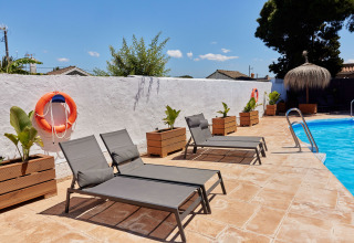 Lettini prendisole presso la piscina di TAIGA Conil, Andalusia, con piante in vaso e salvagenti arancioni.