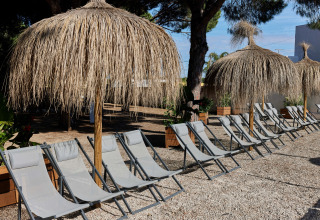 Strandstole under stråtækte parasoller på TAIGA Conil feriepark i Andalusien, Spanien, på en solrig dag.