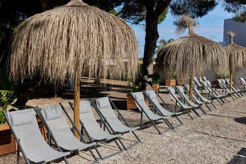 Strandstole under stråtækte parasoller på TAIGA Conil feriepark i Andalusien, Spanien, på en solrig dag.