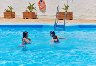 Two girls playing in the swimming pool at TAIGA Conil holiday park in Andalusia, Spain, on a sunny day.