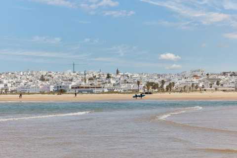 Strandudsigt til TAIGA Conil feriepark i Andalusien, Spanien, med hvidkalkede bygninger og blå himmel.