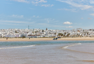 Strandudsigt til TAIGA Conil feriepark i Andalusien, Spanien, med hvidkalkede bygninger og blå himmel.