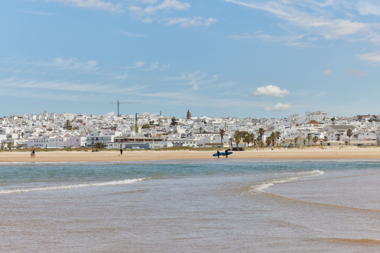 Blick auf den Strand bei TAIGA Conil Ferienpark in Andalusien, Spanien, mit weißen Häusern und blauem Himmel.