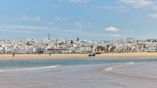 Vista de la playa del parque vacacional TAIGA Conil en Andalucía, España, con casas blancas y cielo azul.