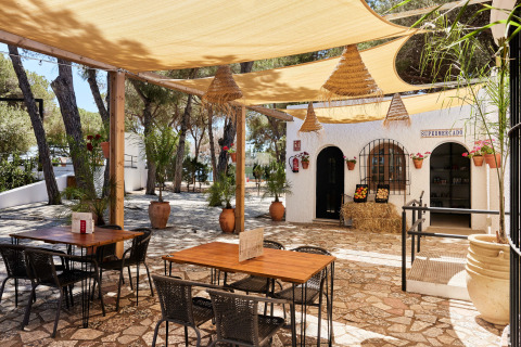 Buitenzitjes met houten tafels en zonneluifels bij TAIGA Conil vakantiepark in Andalusië, Spanje.