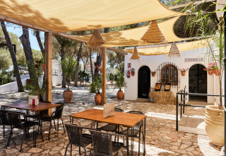 Buitenzitjes met houten tafels en zonneluifels bij TAIGA Conil vakantiepark in Andalusië, Spanje.