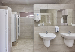 Moderne offentligt badeværelse med to håndvaske, spejl og toiletbåse på TAIGA Conil feriepark i Andalusien.