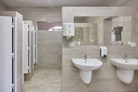 Bagno pubblico moderno nel parco vacanze TAIGA Conil in Andalusia con due lavandini, specchio e cabine.