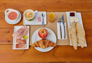 Spansk morgenmad på træbord med kaffe, juice, brød, pålæg, croissant, æble og saucer i Andalusien.