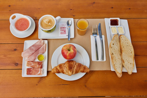 Spanish breakfast on wooden table with coffee, juice, bread, cold cuts, croissant, apple, and sauces in Andalusia.