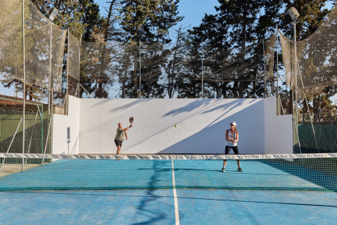To personer spiller tennis på en blå bane omgivet af net ved TAIGA Conil feriepark i Andalusien, Spanien.