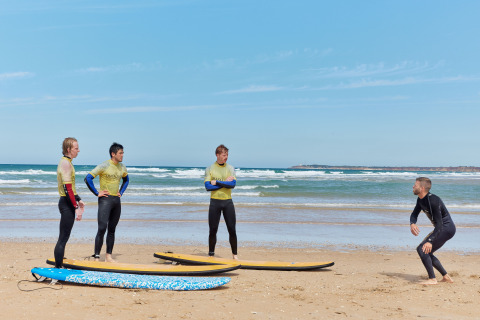 Instructor de surf enseñando a tres participantes en la playa de TAIGA Conil, Andalucía, España.