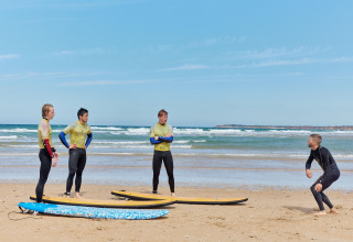 Surfinstructeur geeft uitleg aan drie deelnemers met surfplanken op het strand van TAIGA Conil, Andalusië.