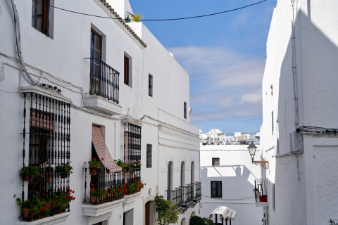 Edificios blancos con balcones y flores en una calle estrecha de TAIGA Conil, Andalucía, España.